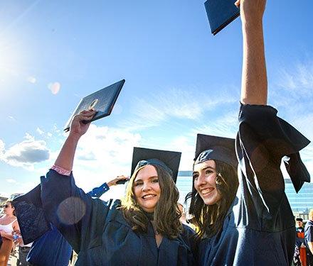 Graduates in gaps and gowns holding up diplomas